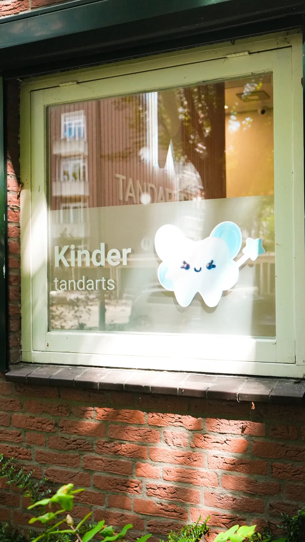 Raamsticker 'Kinder tandarts' met vrolijke tand op het raam van een bakstenen praktijkpand.